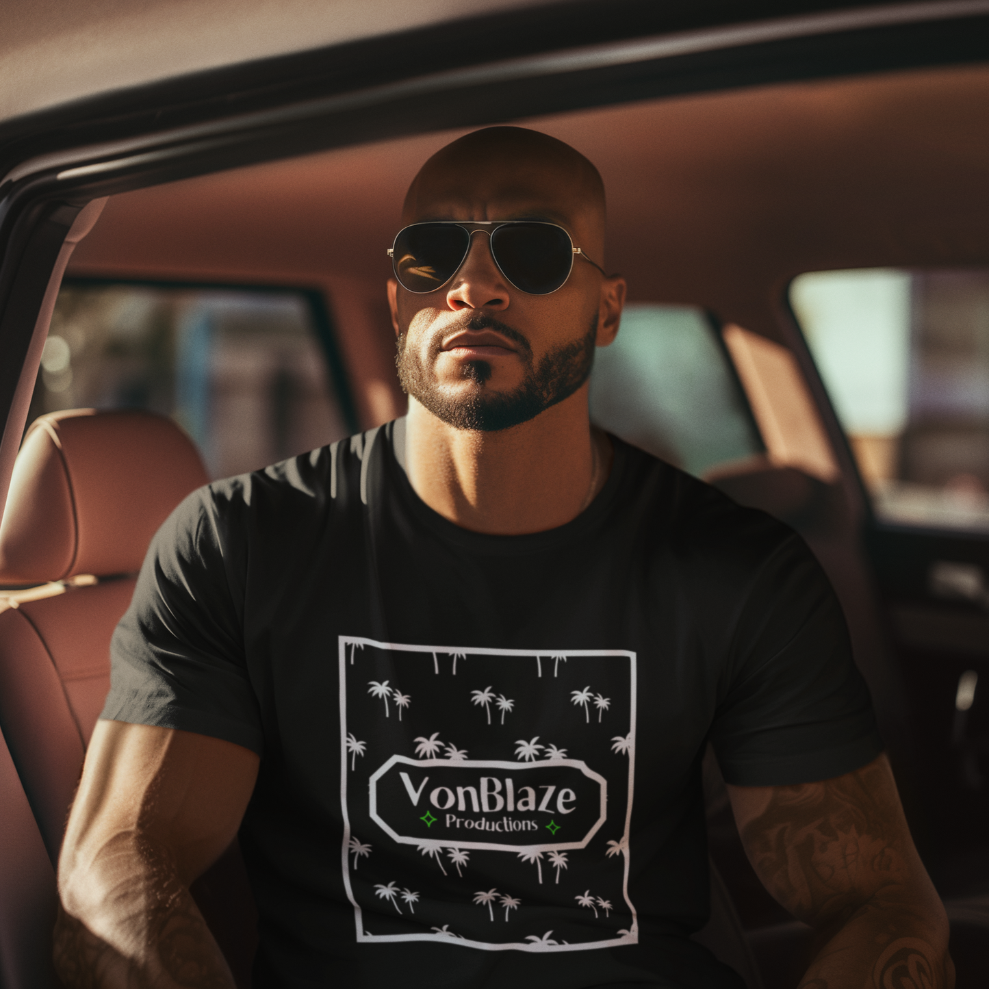 Muscular man sitting in the backseat of a car wearing sunglasses and a black tshirt featuring a square VonBlaze Productions logo with a palm tree patten inside the square